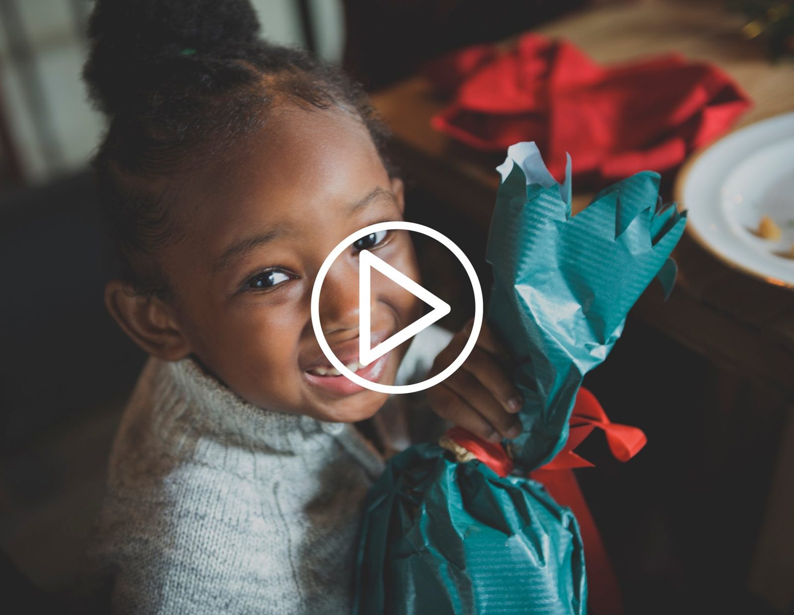 Enfant souriant tenant un cadeau, avec une icône de lecture vidéo